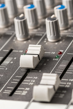 Closeup macro audio mixing console knobs and sliders.