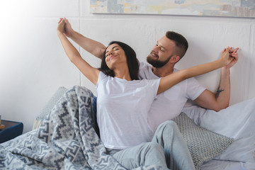 happy young couple holding hands while sitting in bed
