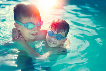 Obraz na płótnie Canvas Happy little kids have fun in swimming pool graded in sunset