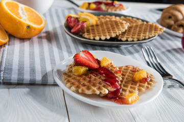 Close-up view of fresh homemade waffles with fruits and jam on table