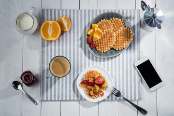Top view of fresh tasty breakfast with waffles and smartphone with blank screen on table