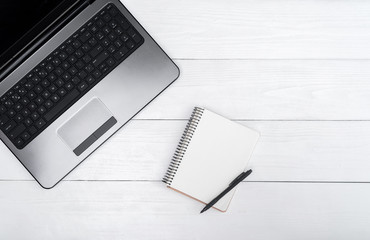 Wooden white office desk table with open blank laptop computer and empty white diary with pen, free space. Top view with copy space. Grey laptop on wooden background