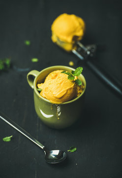 Refreshing summer dessert. Mango sorbet ice cream scoops with fresh mint leaves in green cup over black wooden background. Clean eating, healthy, vegan, weight loss, alkaline diet food concept