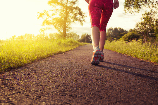 Sportliche Frau joggt einen Weg in der Natur bei Sonnenuntergang entlang - Konzept Sport, Fitness & Motivation 