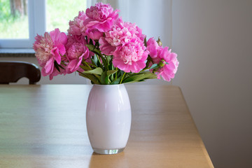 Fresh bouquet of peonies in a glass vase on a wooden table