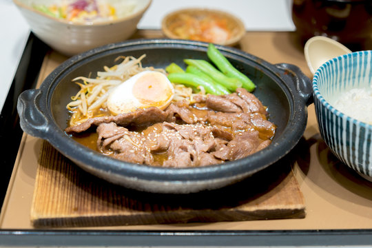 Korean Barbecued Pork in hot pan with egg, sprout and peas on side.