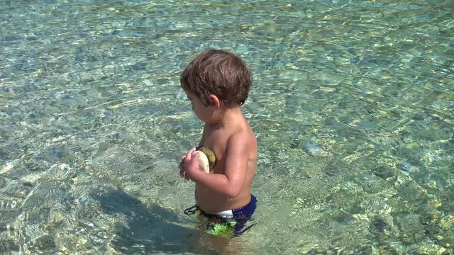 4K Little boy collects stones in the sea 