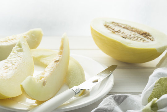 Melon cut into pieces on a white wooden table. A high key.