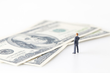 Miniature model of businessman thinking with project for investment standing together on money.