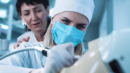 Female student in uniform practicing dentistry on mannequin with instructor.