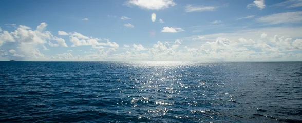 Foto op Plexiglas Een panoramisch tafereel van blauwe lucht en de oceaan met zonnestraal erboven © kevinlert