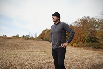 Mature Male Runner Pausing For Breath During Exercise In Woods