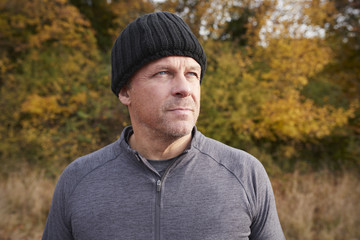 Mature Male Runner Pausing For Breath During Exercise In Woods
