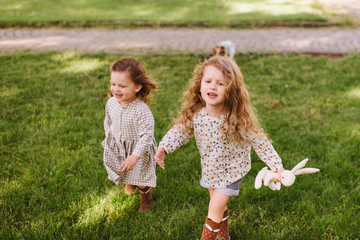 Fototapeta premium Two little cute girls walking on grass in the park in a warm sunny summer day. sisters playing together. Outdoor