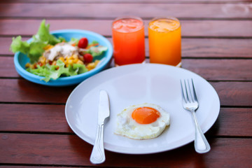 Healthy breakfast with fried egg, tuna salad and juice drink on wooden table.