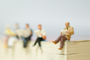 Miniature mini figures businessman sitting and reading on a big book,Improve knowledge and sharing....