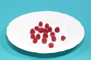 Berries of ripe raspberries on a white plate on a blue background 