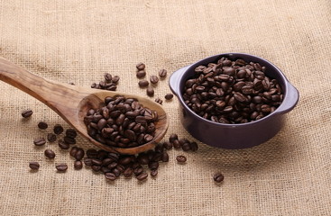 pile coffee beans, wooden spoon and dish on jute background, texture
