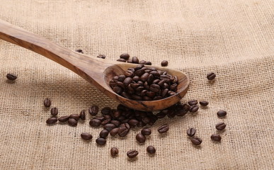 pile coffee beans and wooden spoon on jute background, texture
