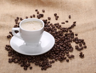 pile coffee beans and white cup on jute background, texture
