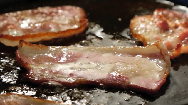 sizzling bacon in black frying pan
