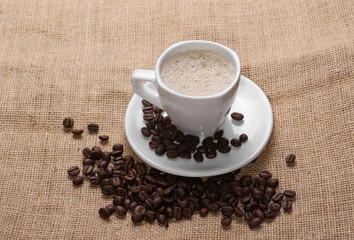 pile coffee beans and white cup on jute background, texture

