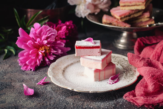 Fruit cakes taffy (lucum) and sand cakes on a dark background, decorated with peonies. Summer light and delicious dessert.