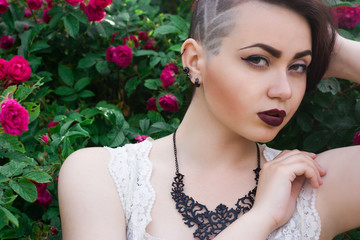 A chic girl in a lace blouse is standing near a bush of roses