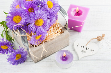 Purple daisies and lit candles on white table