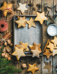 Christmas or New Year background. Gingerbread cookies, sugar powder, nuts, spices, baking molds, fir-tree branch on wooden background, rustic tray with baking paper in center, top view, copy space