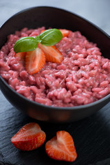Close-up of risotto with strawberries served in a black bowl, selective focus, shallow depth of field