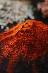 Grounded chili pepper on black rustic surface, surrounded by spices.