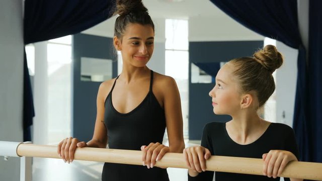 Close Up Portrait Of Young Dance Teacher And Her Student Looking To Each Other And Smiling On Camera In The Ballet Studio.