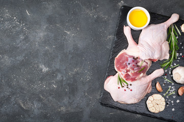 Raw poultry meat. Duck legs with rosemary, spices and olive oil on cutting board over dark background. Ingredients for cooking meat. Top view