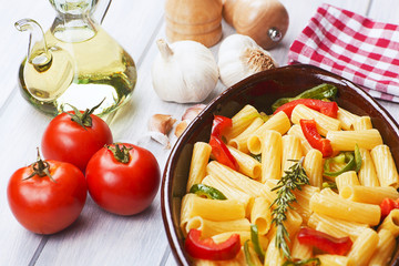 Close-up view of bowl with vegetable pasta served on table with fresh tomatoes and garlic.
