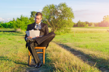 Naklejka na ściany i meble A man in a suit is studying documents sitting among nature, work on vacation.
