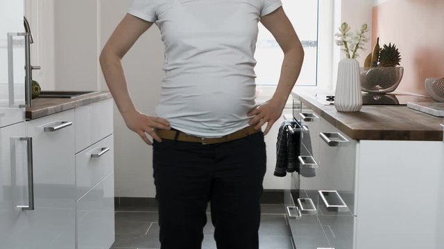 A pregnant woman wearing a white t-shirt and black pants dances in her kitchen. A medium profile shot of her body as she sways her hips and jumps up and down.
