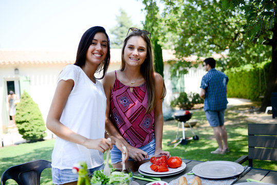 two beautiful young woman in garden preparing tomato salad for barbecue party during summer holiday