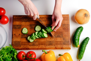 Woman cutting fresh cucumber on wooden board ingredients for salad