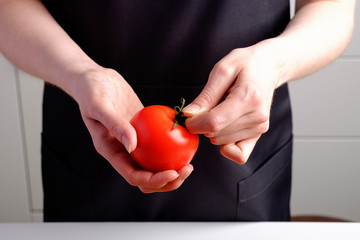 Woman hand holding tomato at kitchen background. in black apron