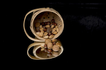 different nuts spilling out of a basket onto a reflective surface with black background 