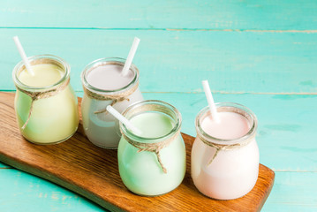 Small jars with a multi-colored smoothie or milkshake - pink cherry, purple berry, green and yellow orange. On a light blue wooden table copy space