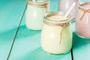 Small jars with a multi-colored smoothie or milkshake - pink cherry, purple berry, green and yellow orange. On a light blue wooden table copy space