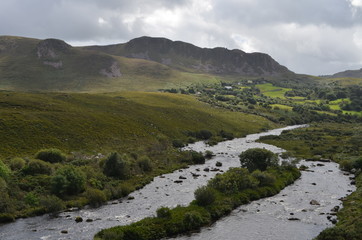 Fototapeta na wymiar Small River Flow in Green Vegetation and Mountain Landscape in a National Road in Ireland