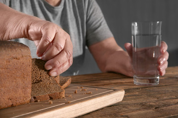 Elderly woman pinching off a piece of bread at table. Poverty concept