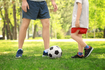 Father and son playing football on green grass in park