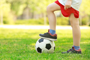 Legs of little boy with soccer ball in green park on sunny day