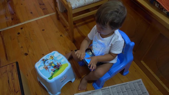 4K Child playing with tablet sitting on potty