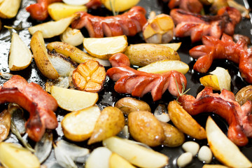 Homemade traditional sausages and potatoes in a black frying pan.