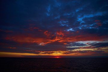 Naklejka na ściany i meble Amazing sunrise over dark sea with deep blue and red colors